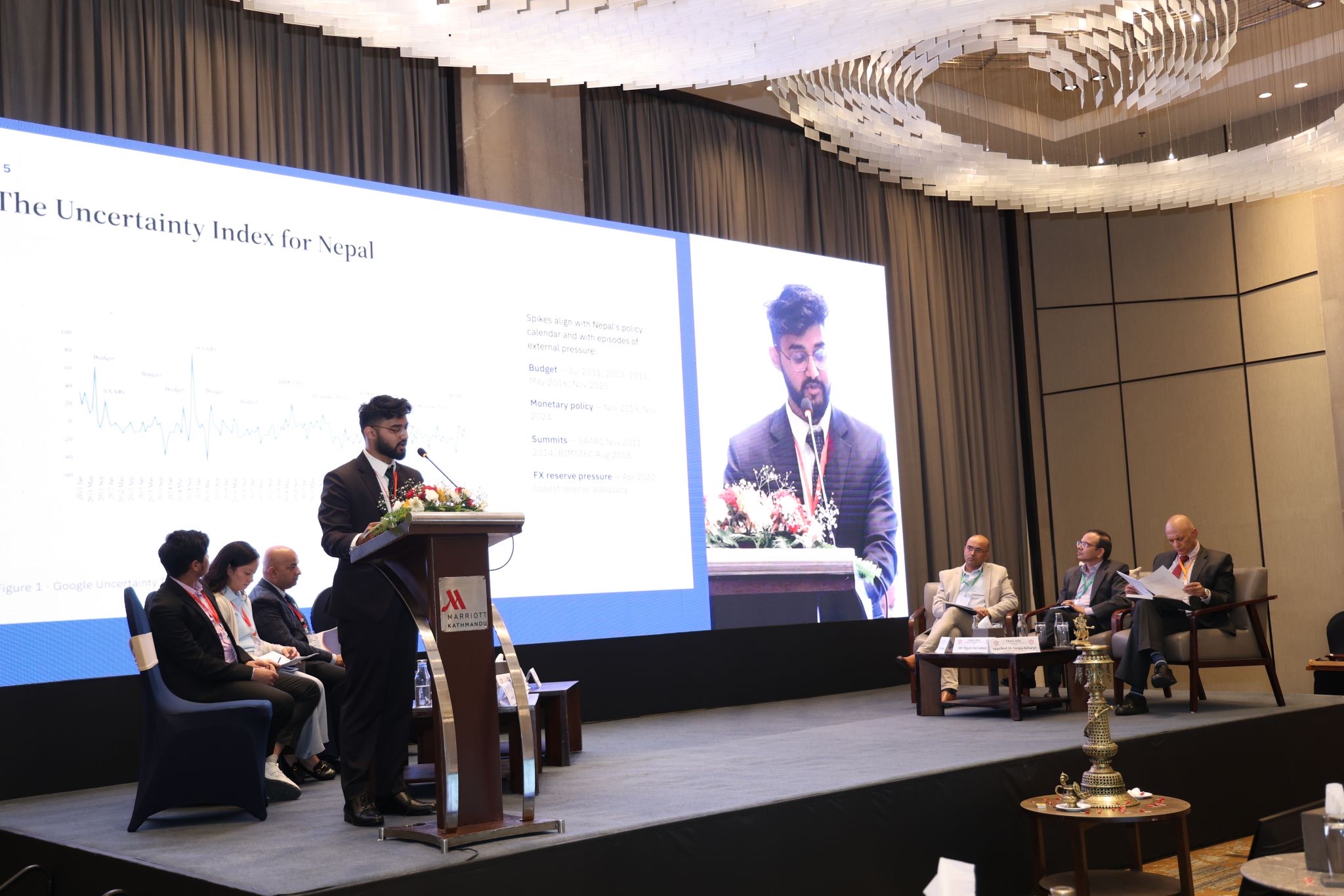 Swostik Nepal presenting the Economic Policy Uncertainty index for Nepal on stage at CAICE 2026, with the slide on the main screen